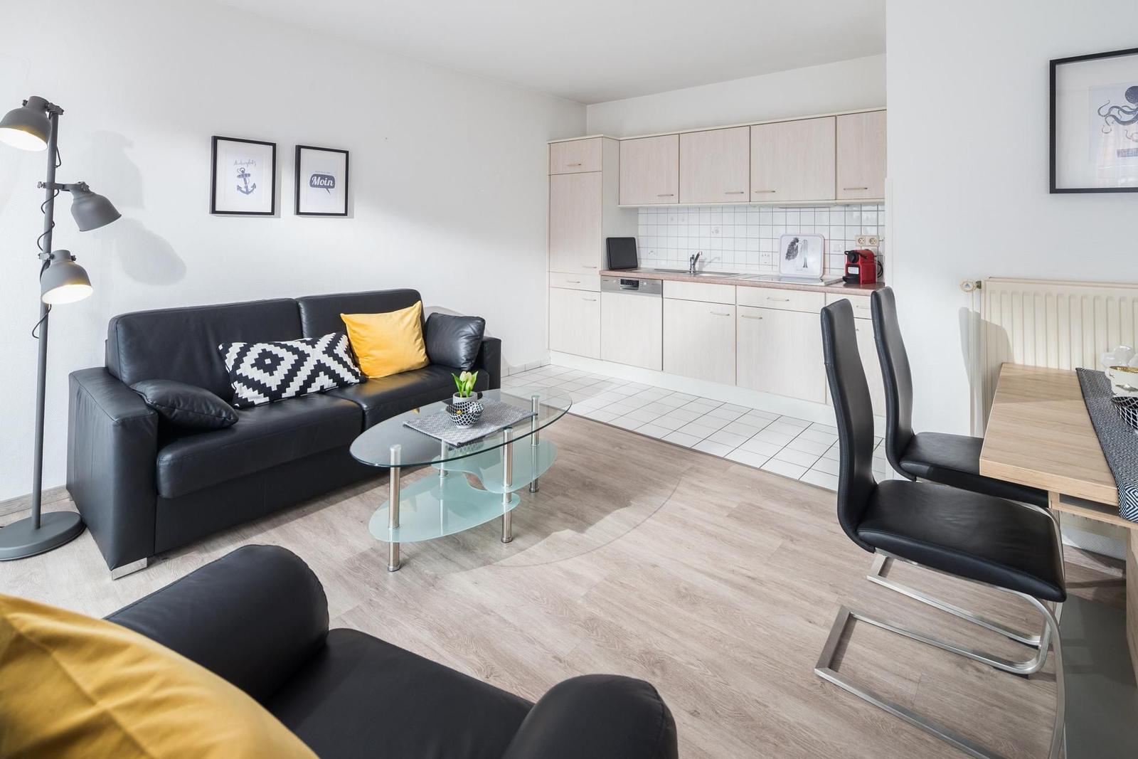 Wohnbereich mit Sofa, Esstisch und Küche im Hintergrund.