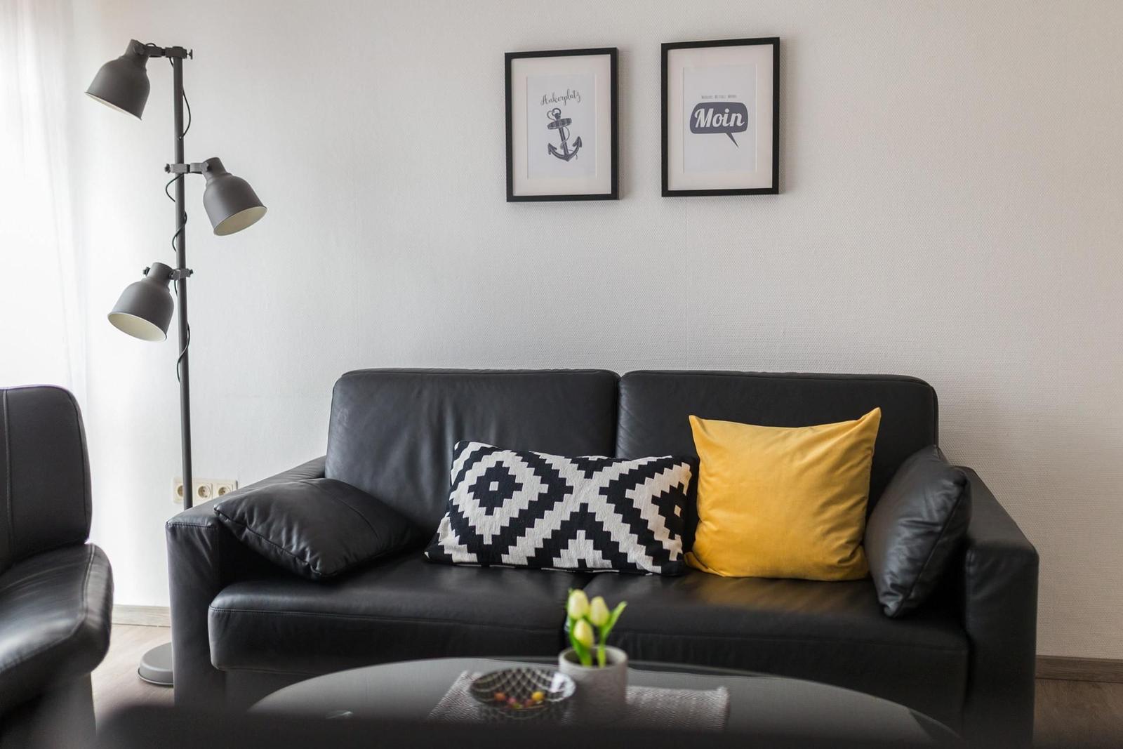 Schwarzes Sofa mit Kissen, Stehlampe und Wandbildern.