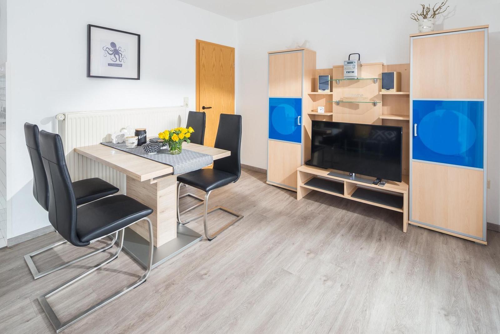 Essbereich mit Tisch und Stühlen. Fernseher und Schränke im Wohnbereich.
