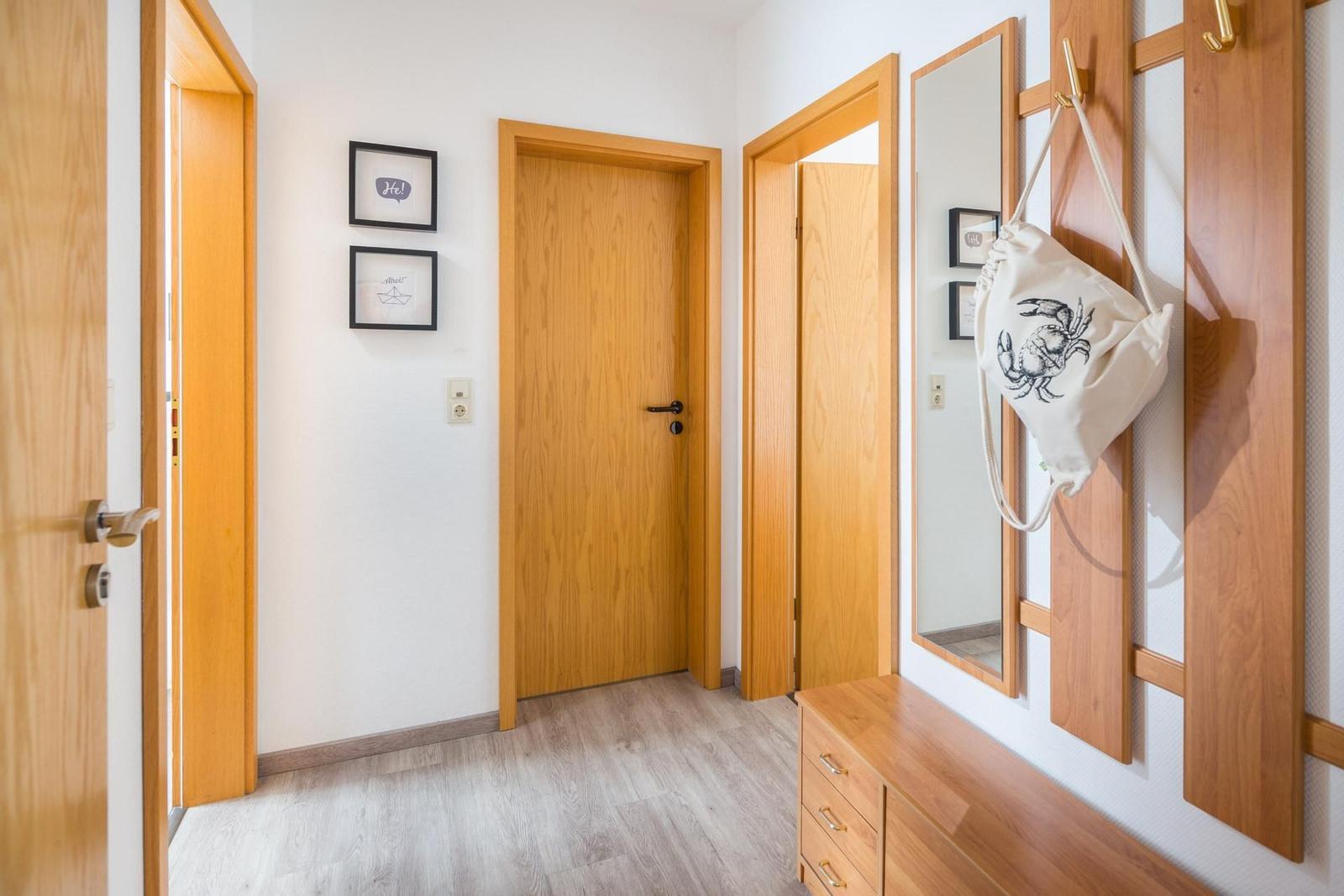Flur mit Holztüren, Spiegel und Kleiderhaken. Wandbilder und Holzschrank sind sichtbar.