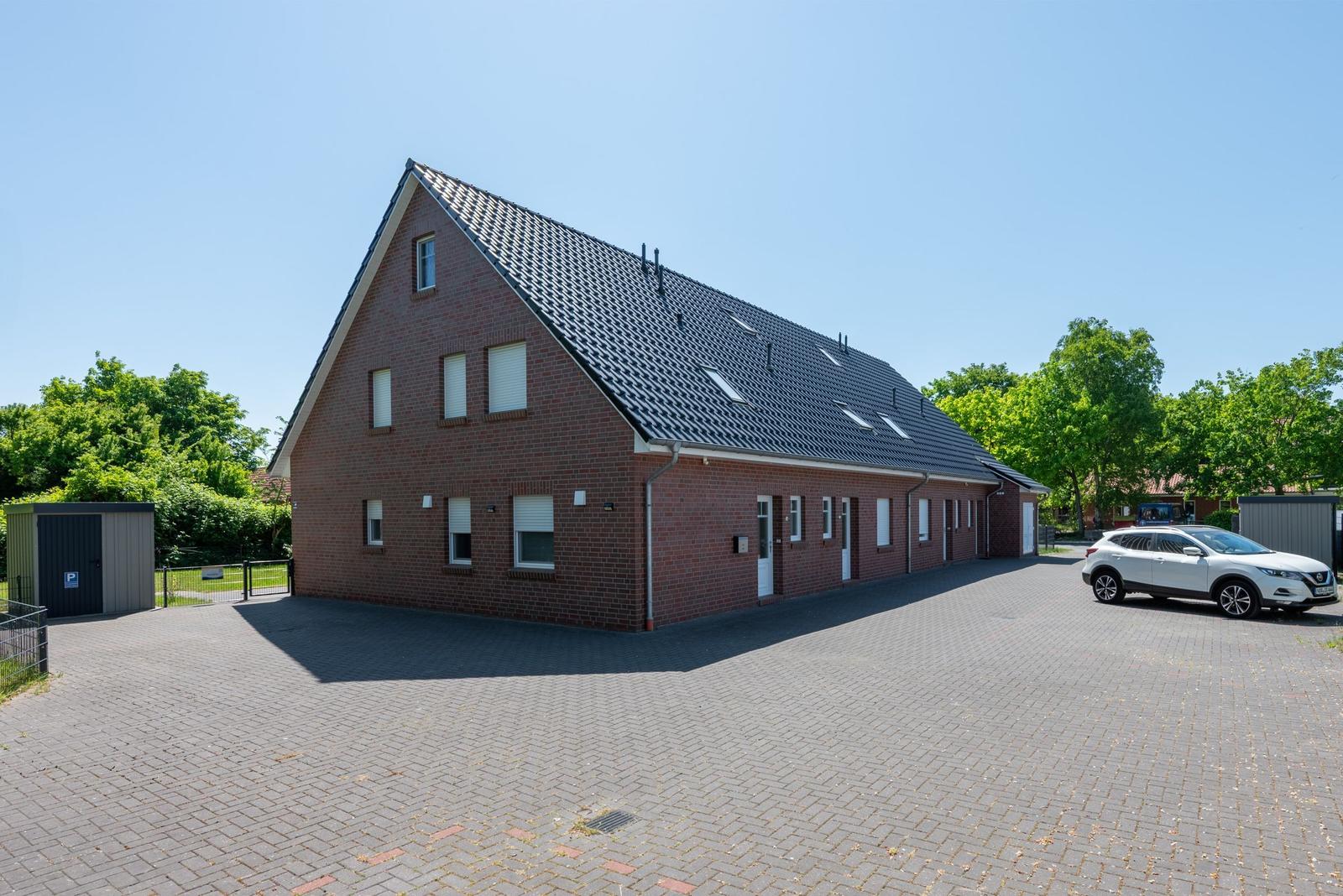 Rotes Backsteingebäude mit Dachfenstern und gepflastertem Hof. Ein weißes Auto steht vor dem Haus.