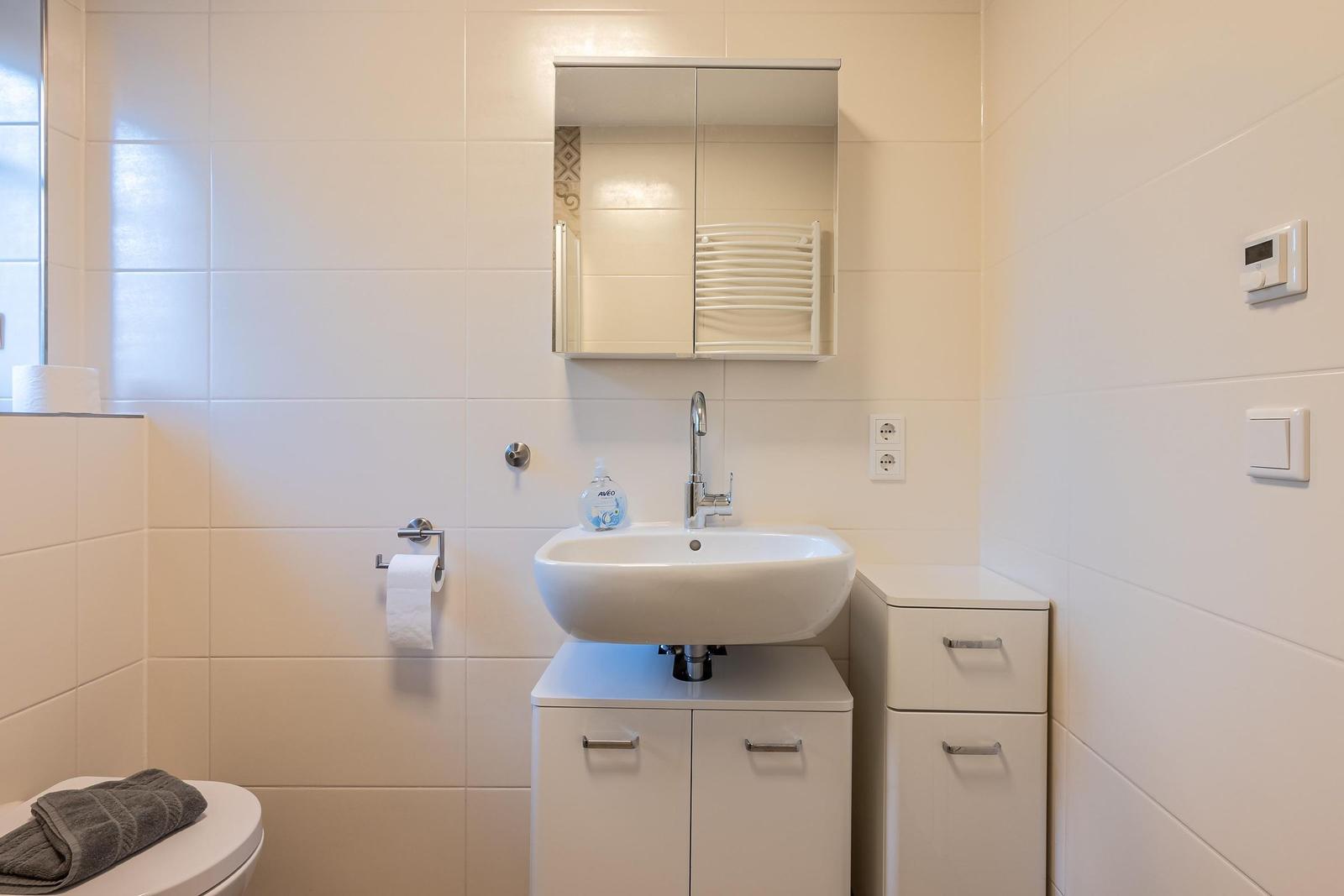 Badezimmer mit Waschbecken, Spiegel, Toilette und Handtuchhalter.