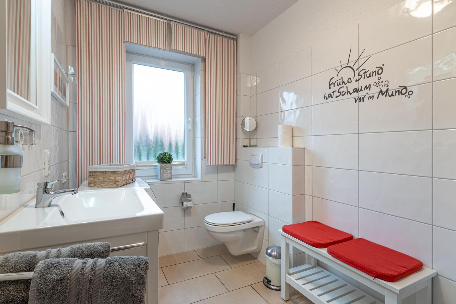 Badezimmer mit Toilette, Waschbecken und rotem Sitzbank