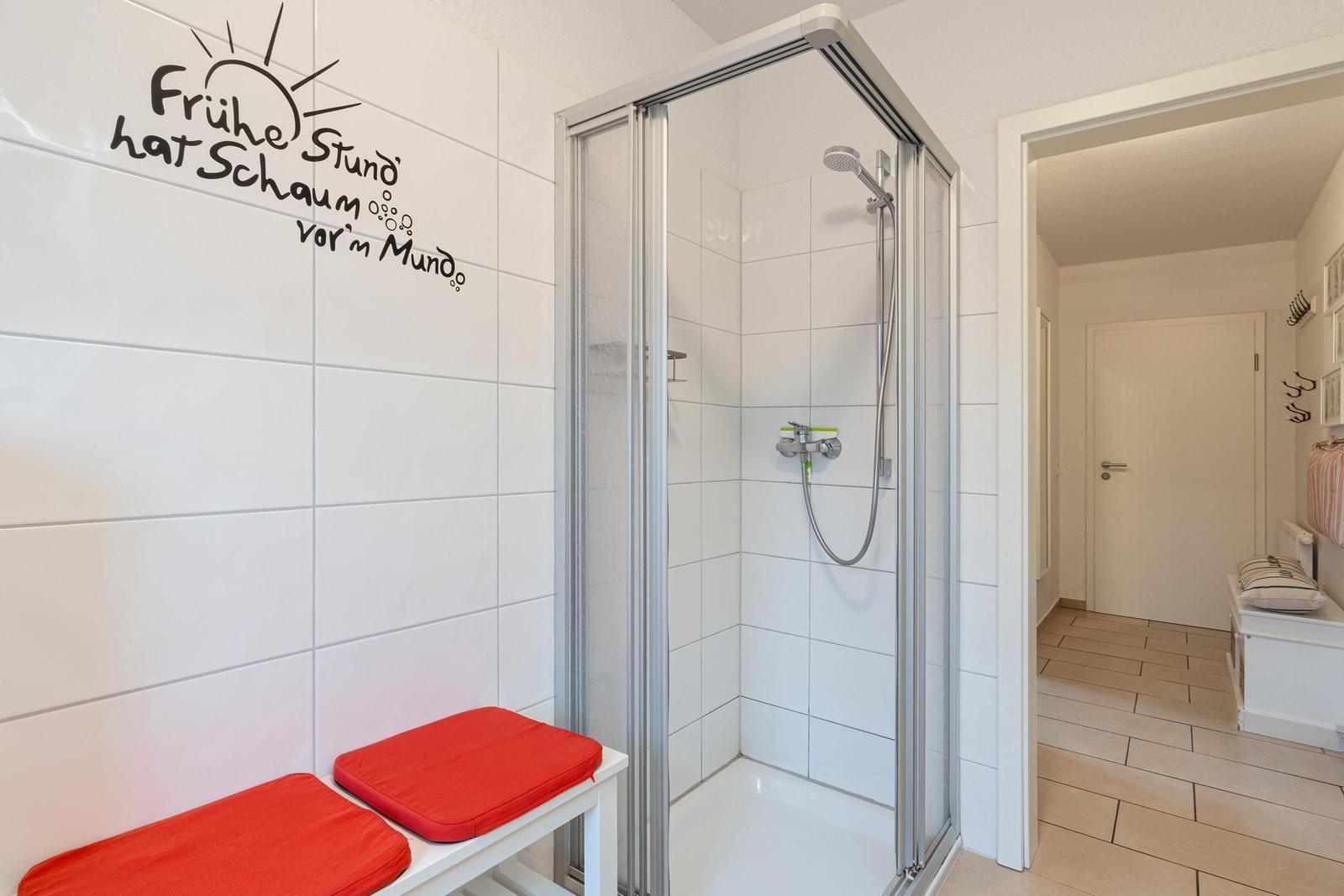 Duschbereich mit Duschkabine und roten Sitzkissen an der Wand.