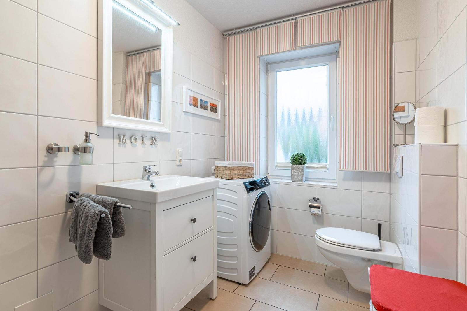 Badezimmer mit Waschmaschine, Toilette und Fenster mit Streifenrollo.