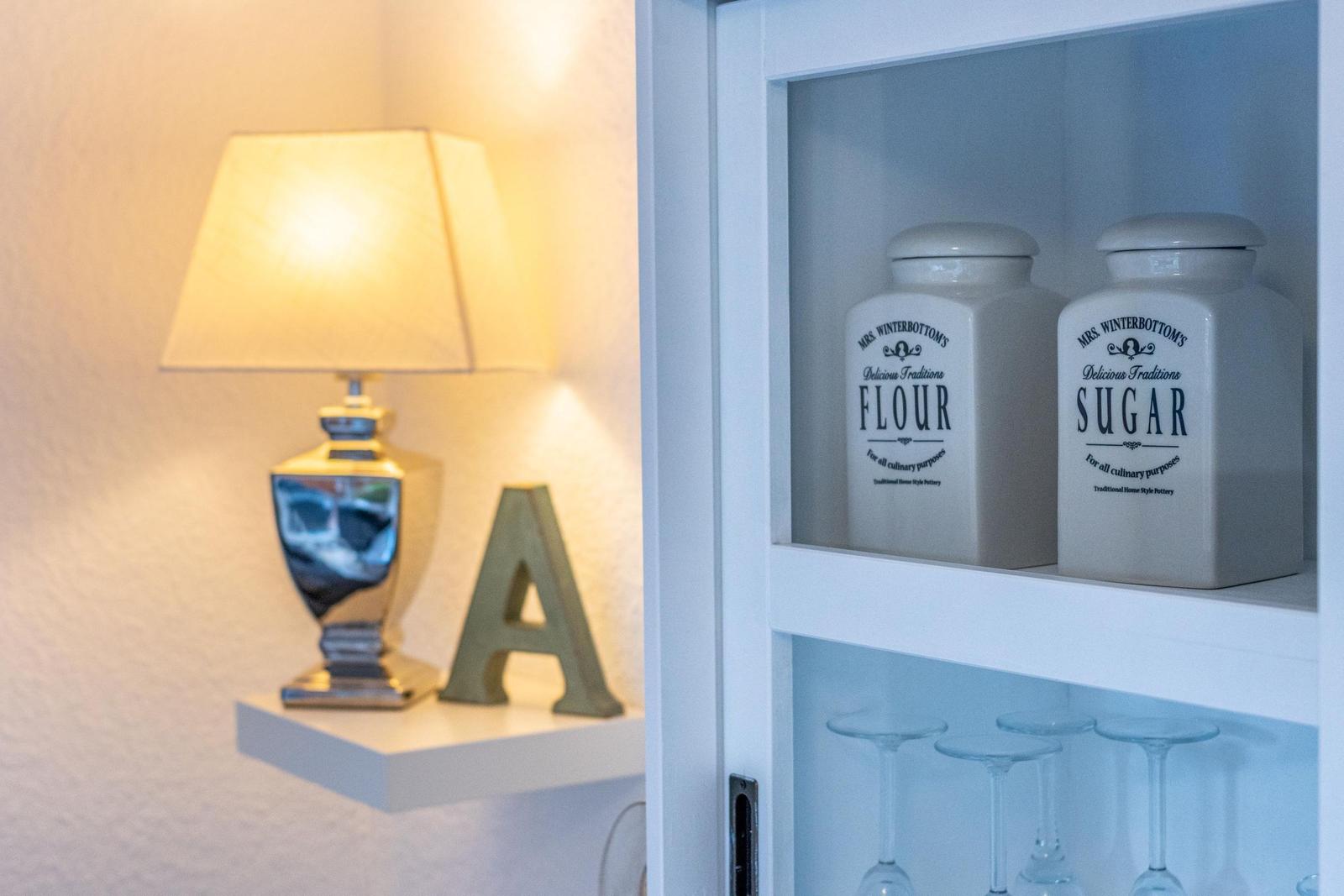 Schrank mit Mehl- und Zuckerkanistern, Lampe und Buchstaben-A auf Regal.