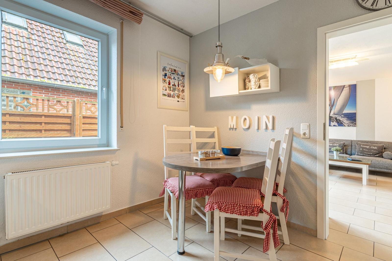 Essbereich mit runden Tisch, weißen Stühlen und rot-weißen Sitzkissen. Durchgang zum Wohnzimmer.
