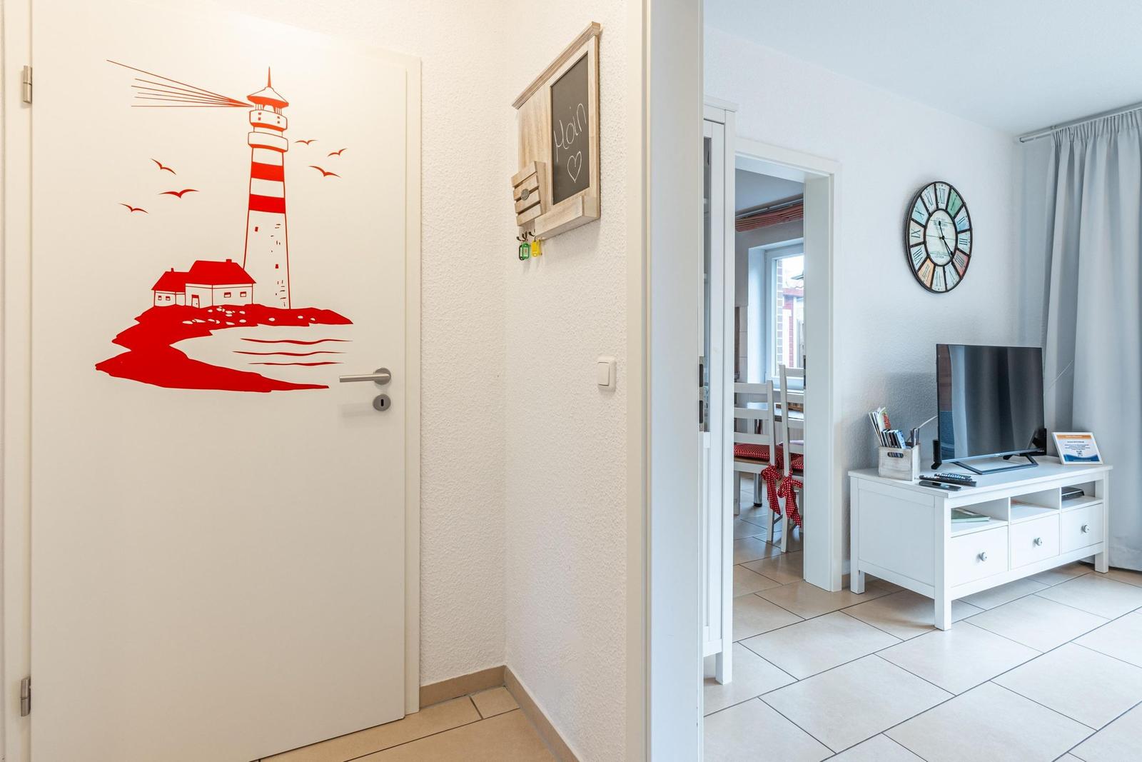 Eingangsbereich mit rotem Leuchtturm-Aufkleber. Durchgang in Wohnzimmer mit Fernseher und Uhr.