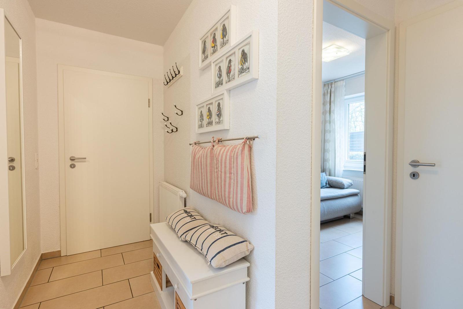 Eingangsbereich mit Kleiderhaken, Bildern und Sitzbank. Durchgang zu Wohnzimmer mit Sofa.