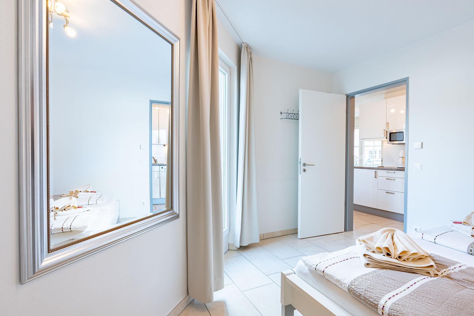 Schlafzimmer mit Spiegel, Bett und Blick in Küche.