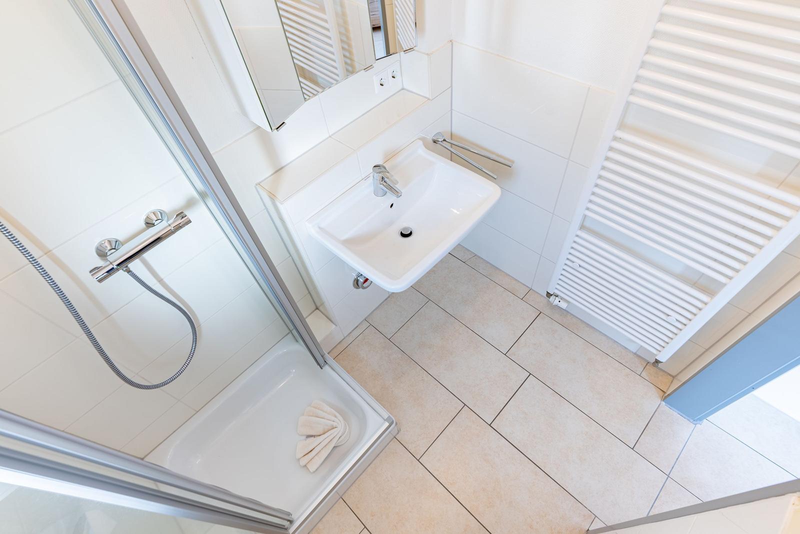 Dusche mit Duschbrause, Waschbecken und Heizkörper.