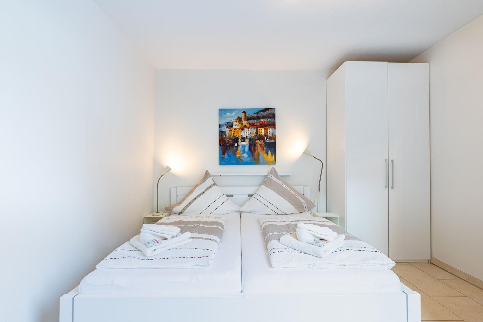 Schlafzimmer mit Doppelbett, Wandbild und Kleiderschrank.
