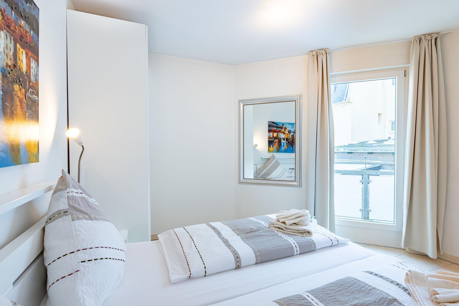 Schlafzimmer mit Bett, Fenster und Wandbild. Decke und Kissen sind gestreift.