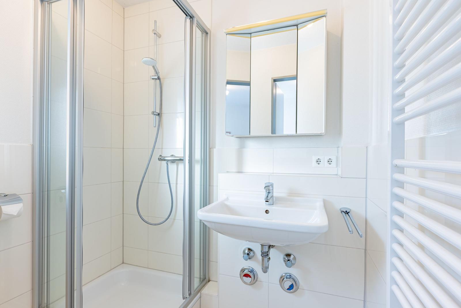 Badezimmer mit Dusche, Waschbecken und Spiegelschrank.