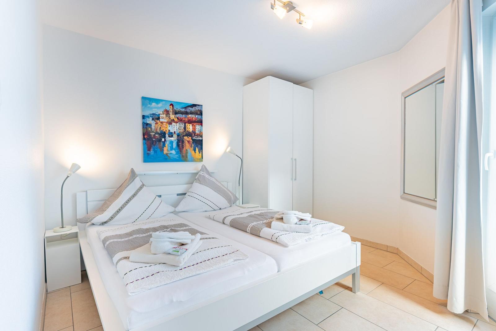 Schlafzimmer mit Doppelbett, Kleiderschrank und Wandbild.