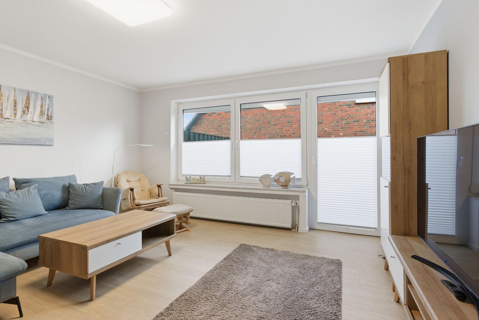 Wohnzimmer mit Sofa, Couchtisch und TV. Fenster mit Jalousien und Wandbild.