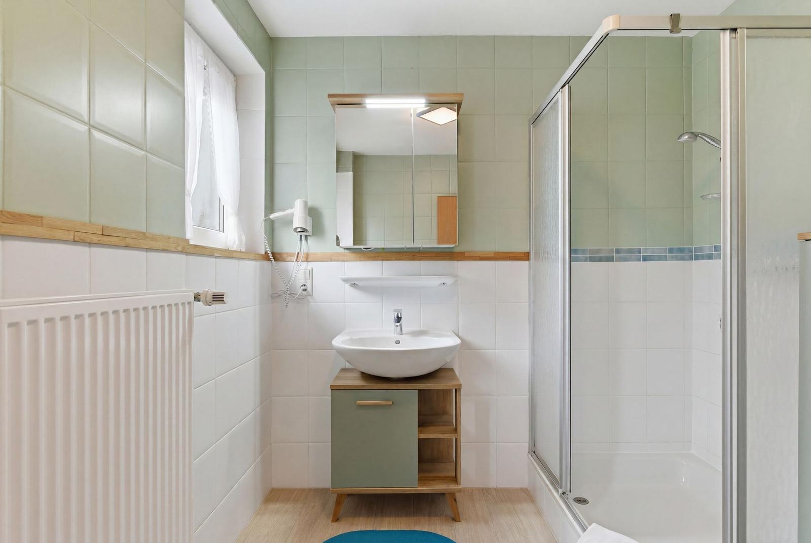 Badezimmer mit Dusche, Waschbecken und Spiegel.