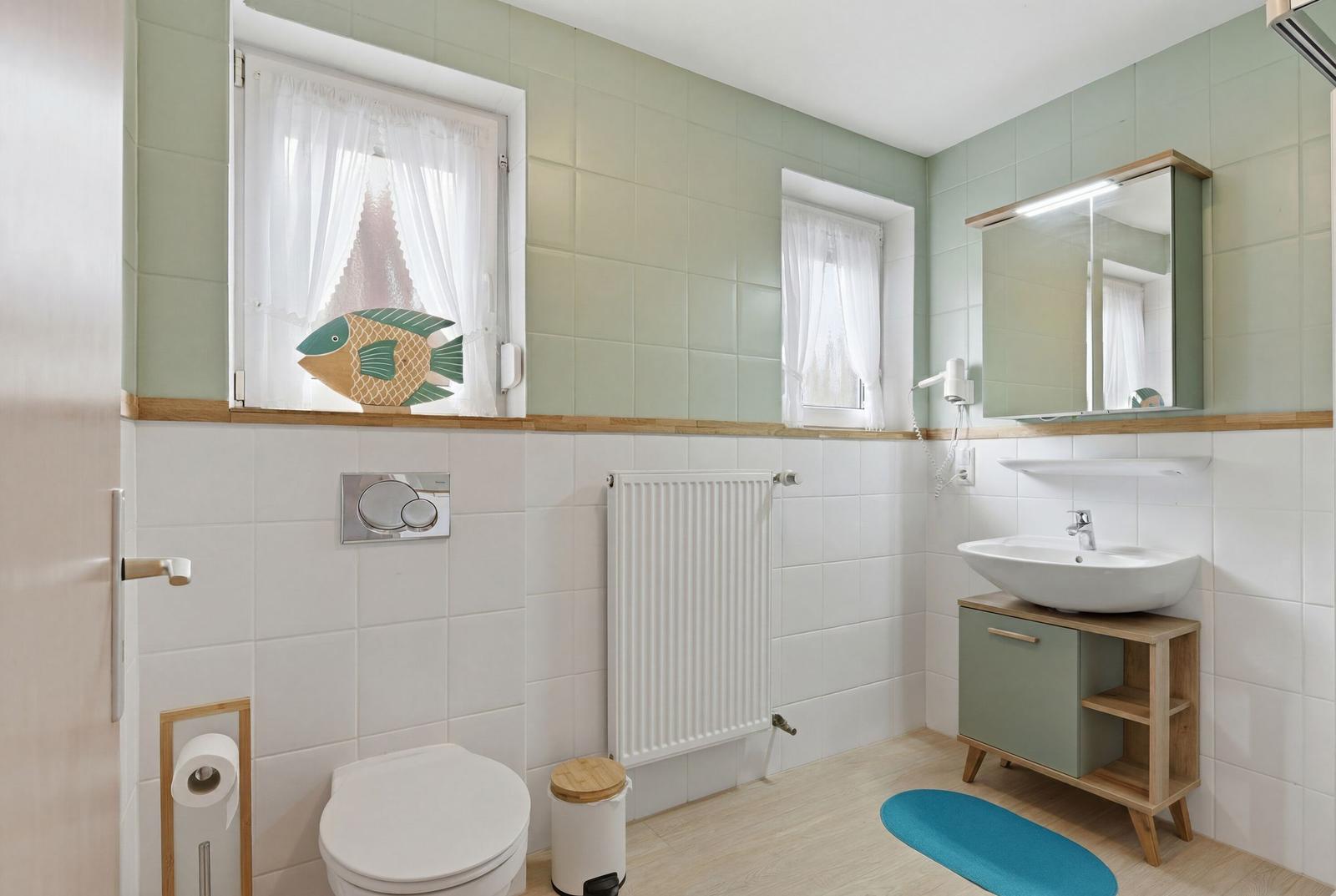 Badezimmer mit Toilette, Waschbecken und Badewanne. Fenster mit Fischmotiv.