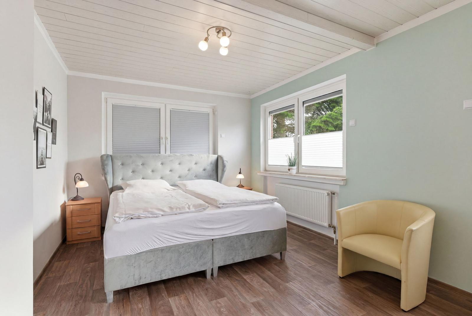 Schlafzimmer mit Doppelbett, gelber Sessel und Holzboden.