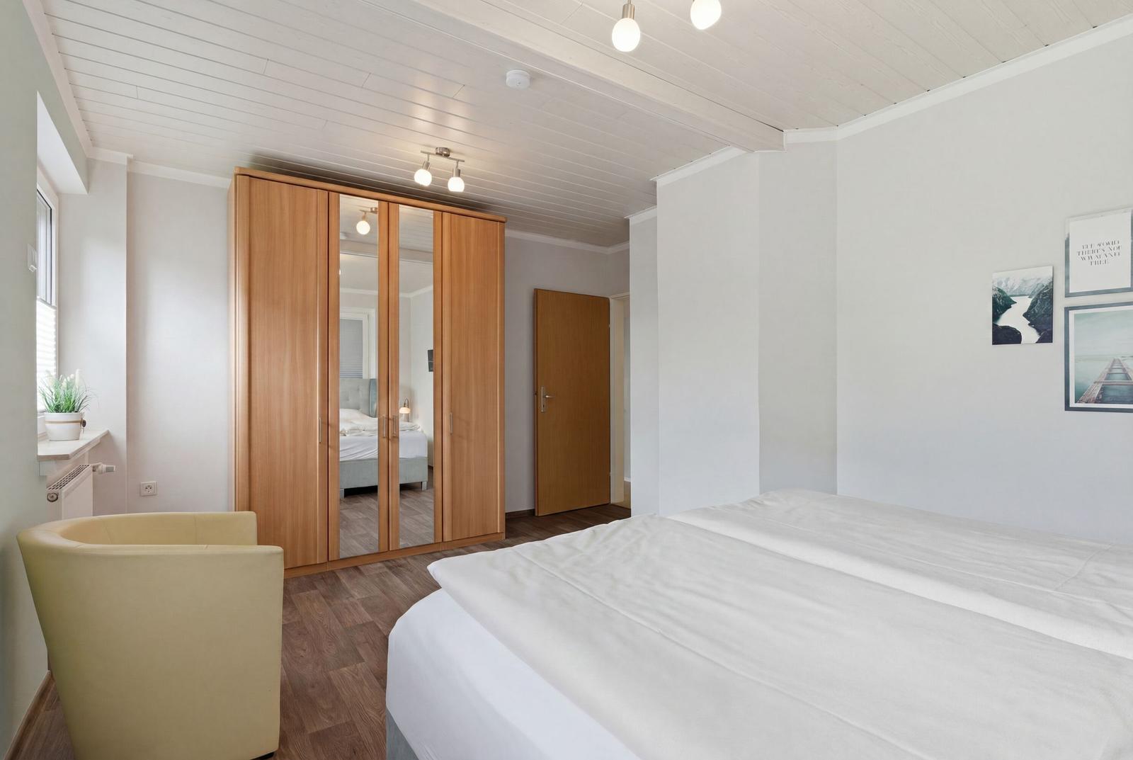 Schlafzimmer mit Bett, Kleiderschrank und Sessel. Wandbilder und Holzboden.