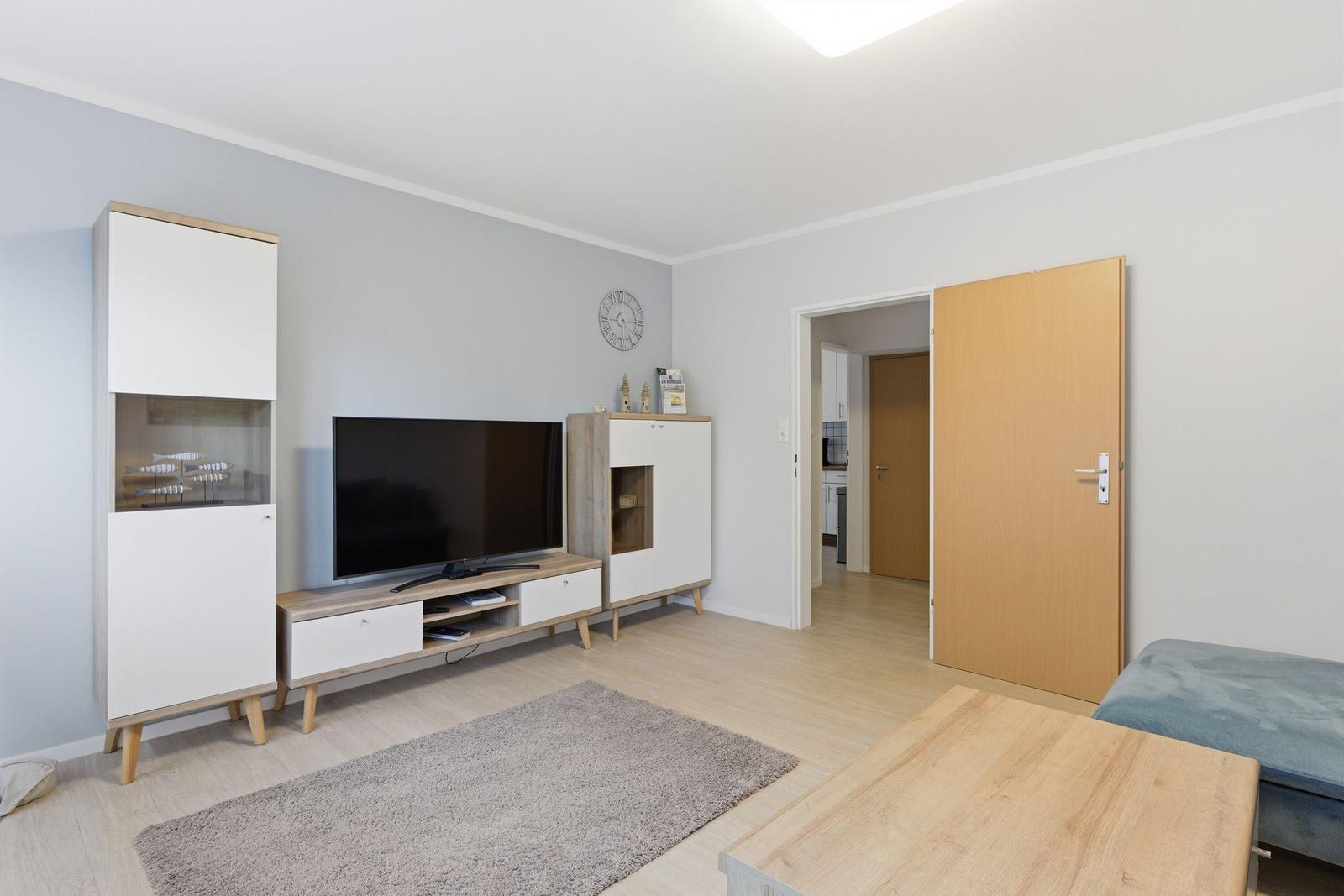 Wohnzimmer mit Fernseher, Holzmöbeln und Tür zum Flur.
