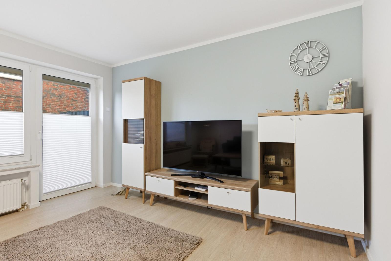 Wohnzimmer mit Fernseher, Schränken und Fenster zur Straße.