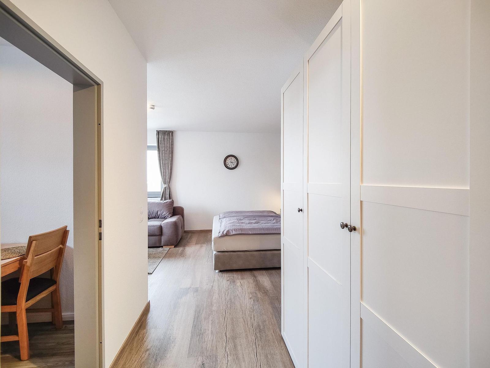 Schlafzimmer mit Bett, Sofa und Kleiderschrank. Holzboden und Wanduhr sichtbar.