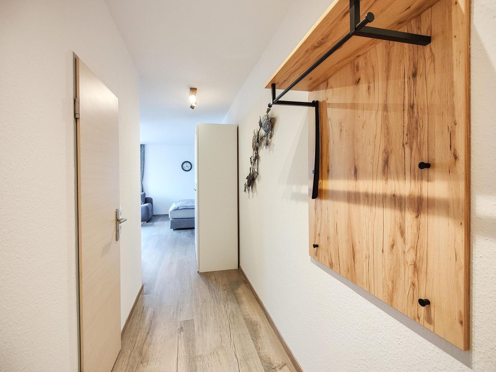 Flur mit Holzwand und Tür. Im Hintergrund ist ein Schlafzimmer mit Bett und Sofa.