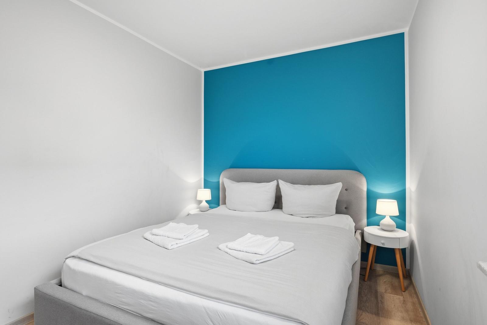 Schlafzimmer mit Bett, blauer Wand und Nachttischen mit Lampen.
