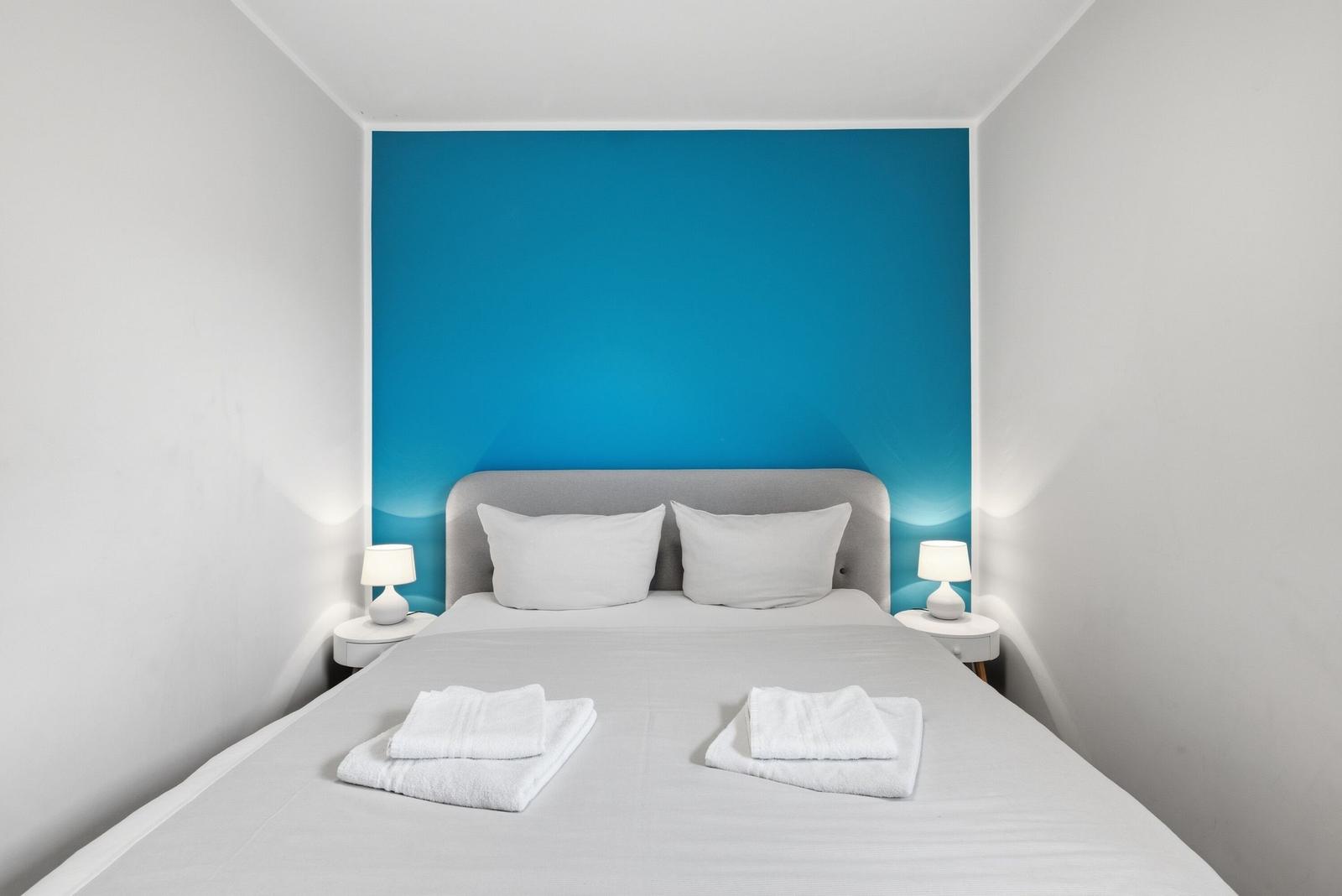 Schlafzimmer mit Bett, zwei Nachttischen und blauer Wand hinter dem Kopfteil.
