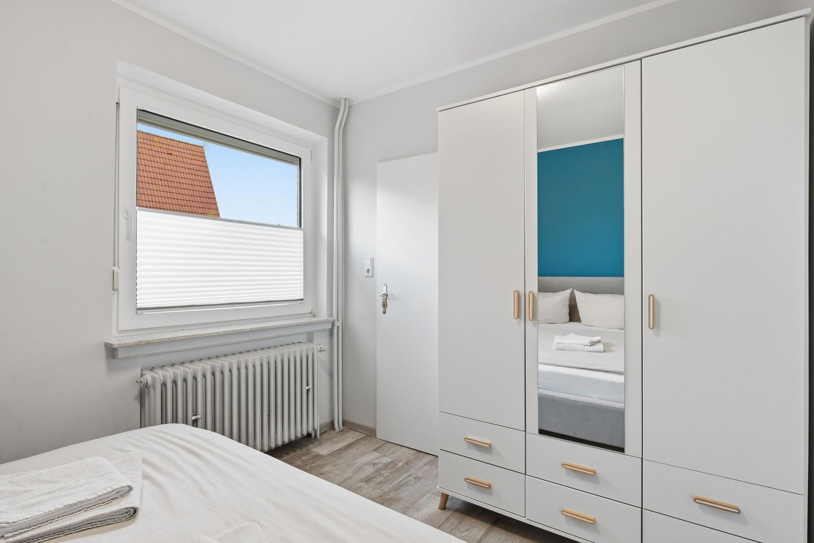 Schlafzimmer mit weißem Schrank, Bett und Fenster mit Blick auf Dach.