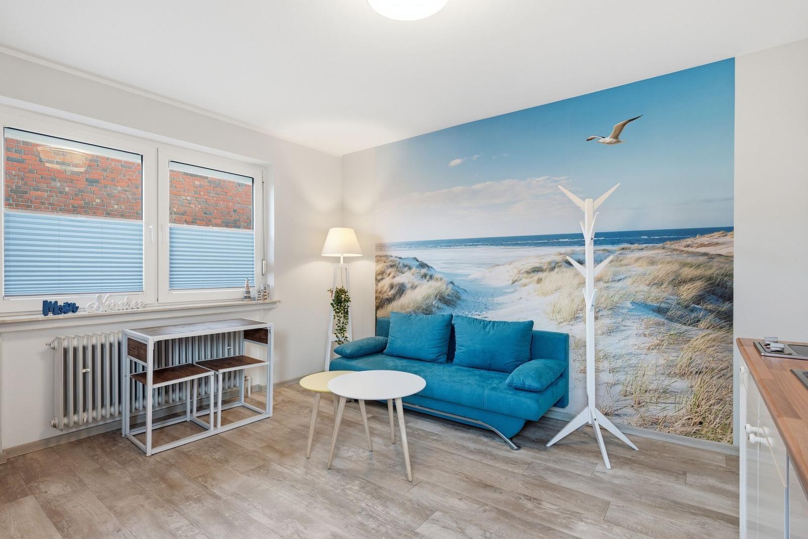 Wohnzimmer mit blauem Sofa, Wandbild Strand und Fenster mit Jalousien.