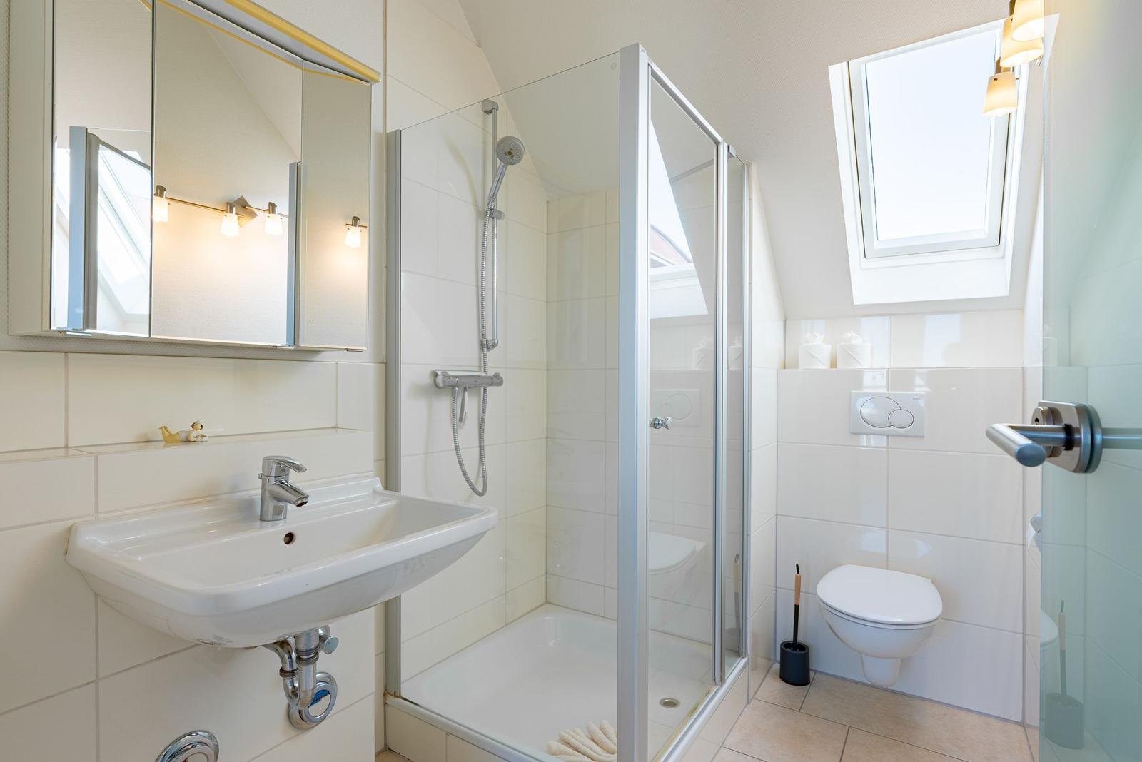 Badezimmer mit Dusche, Waschbecken und WC. Fenster sorgt für Tageslicht.