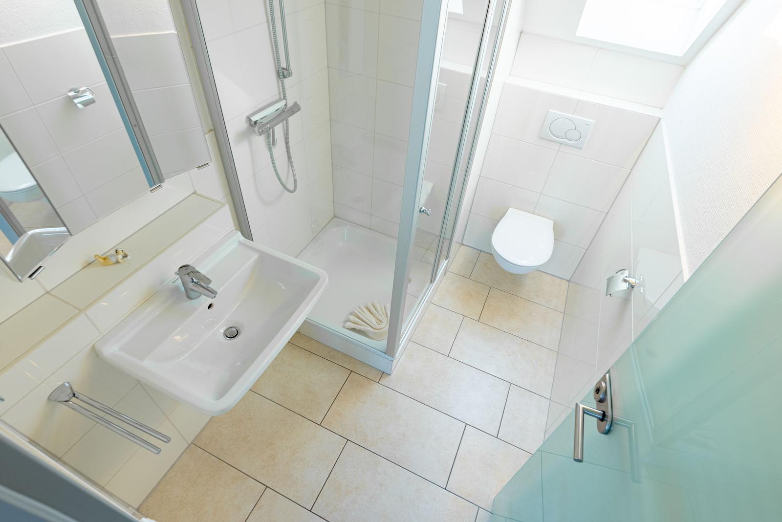 Badezimmer mit Dusche, WC und Waschbecken. Fliesenboden und Spiegel.