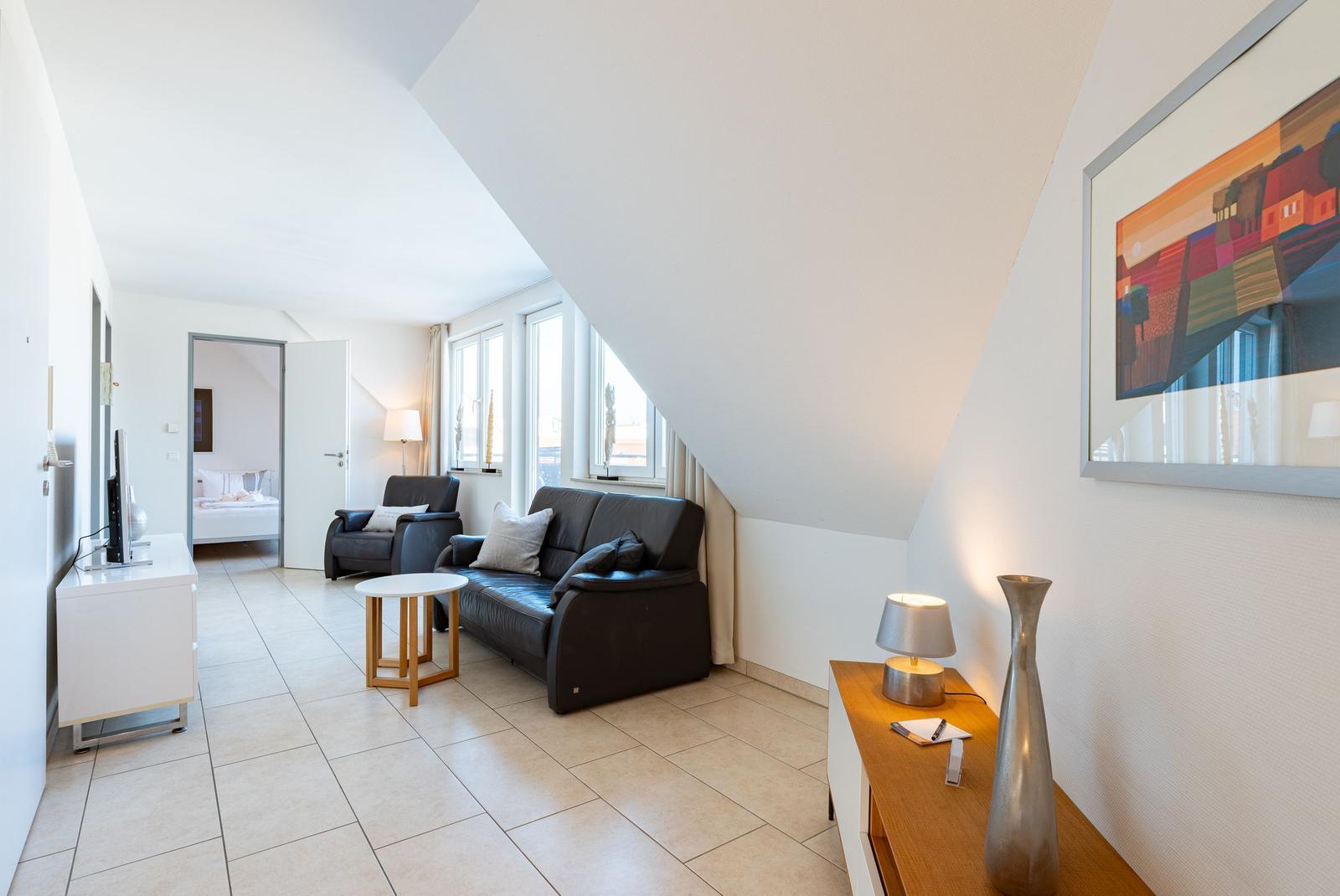Wohnzimmer mit Sofa, Sessel und TV. Durchgang zur Schlafzimmer.