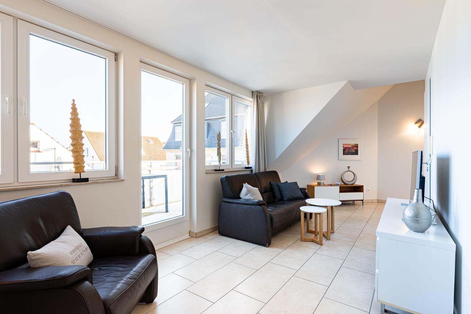 Wohnzimmer mit braunen Ledersofas, großen Fenstern und weißem Bodenbelag.