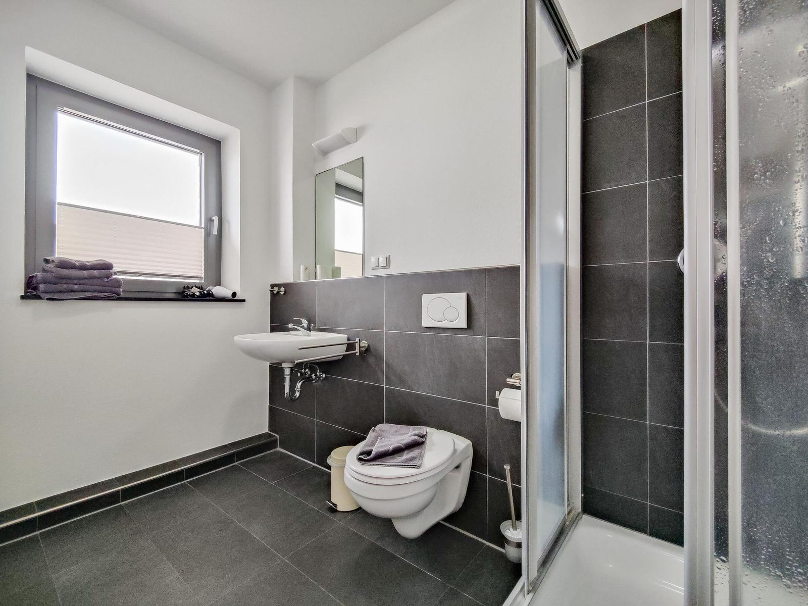 Badezimmer mit Dusche, Toilette und Waschbecken. Fenster mit Handtüchern.
