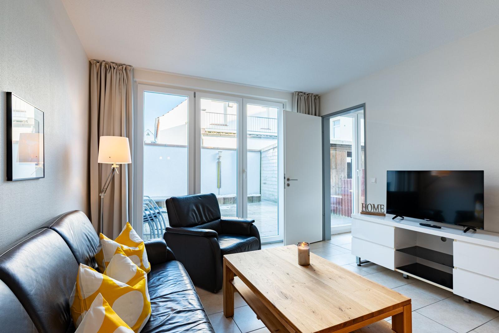 Wohnzimmer mit Sofa, Sessel, Couchtisch und TV. Durchgang zur Terrasse.