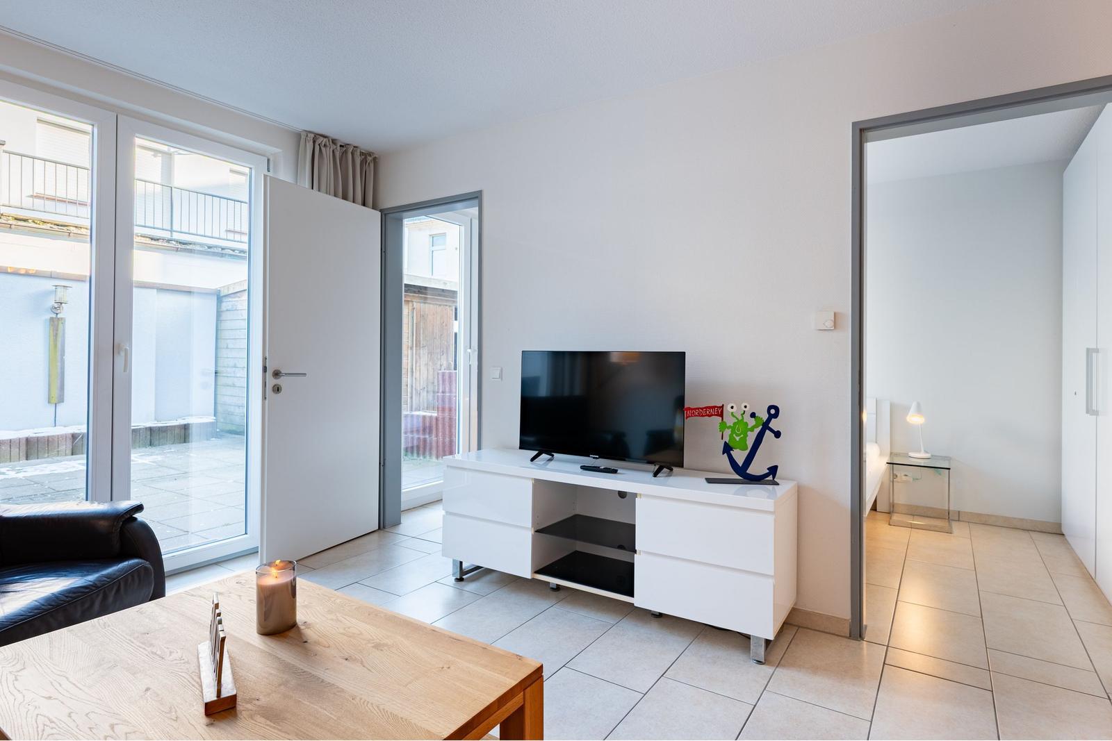 Wohnzimmer mit TV, Couch und Blick auf Balkon. Durchgang zur Schlafzimmer.