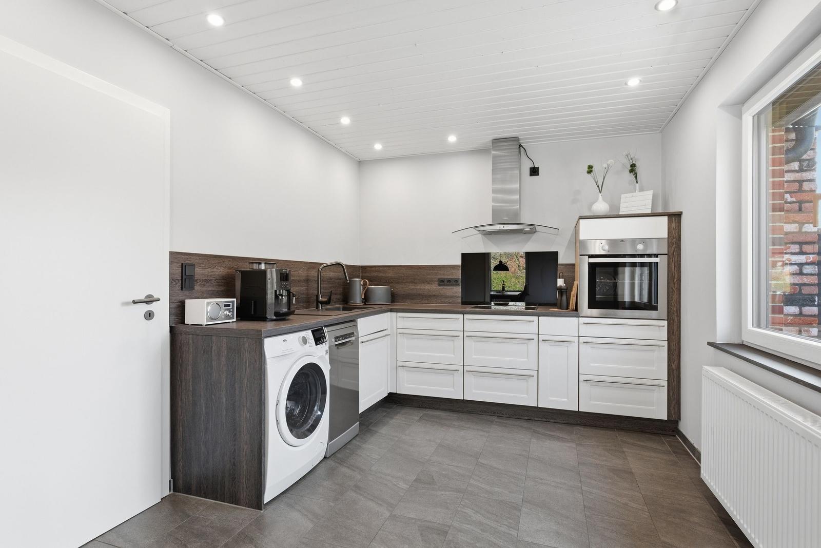 Moderne Küche mit weißer Einbauküche, Edelstahlgeräten und Waschmaschine.