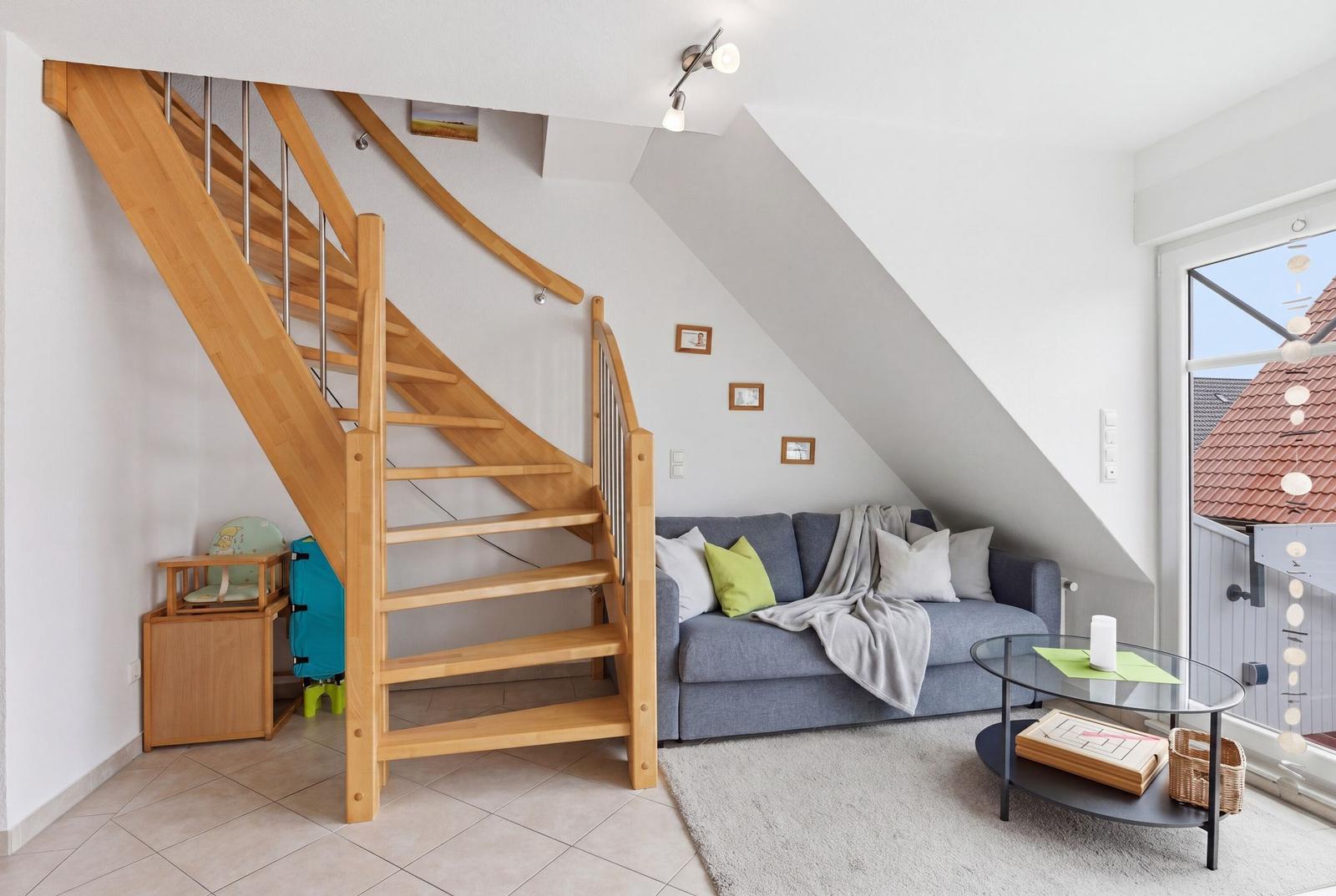 Wohnzimmer mit Sofa, Glas-Tisch und Holztreppe unter Dachschräge