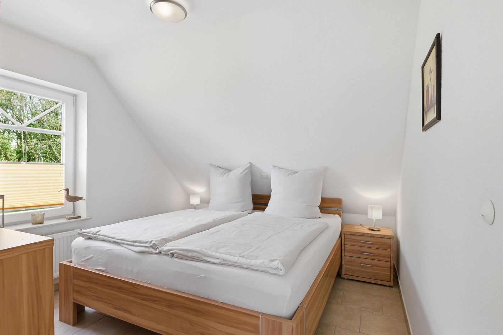 Schlafzimmer mit Doppelbett, Nachttisch und Fenster mit Blick auf Grün.