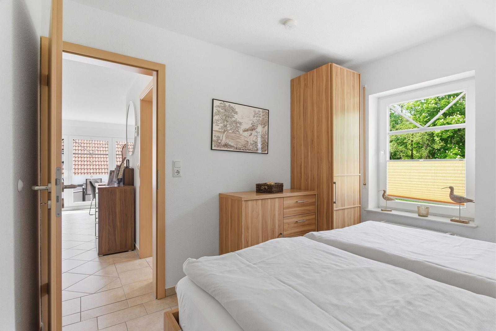 Schlafzimmer mit Doppelbett, Holzschrank und Fenster mit Blick auf Grün.