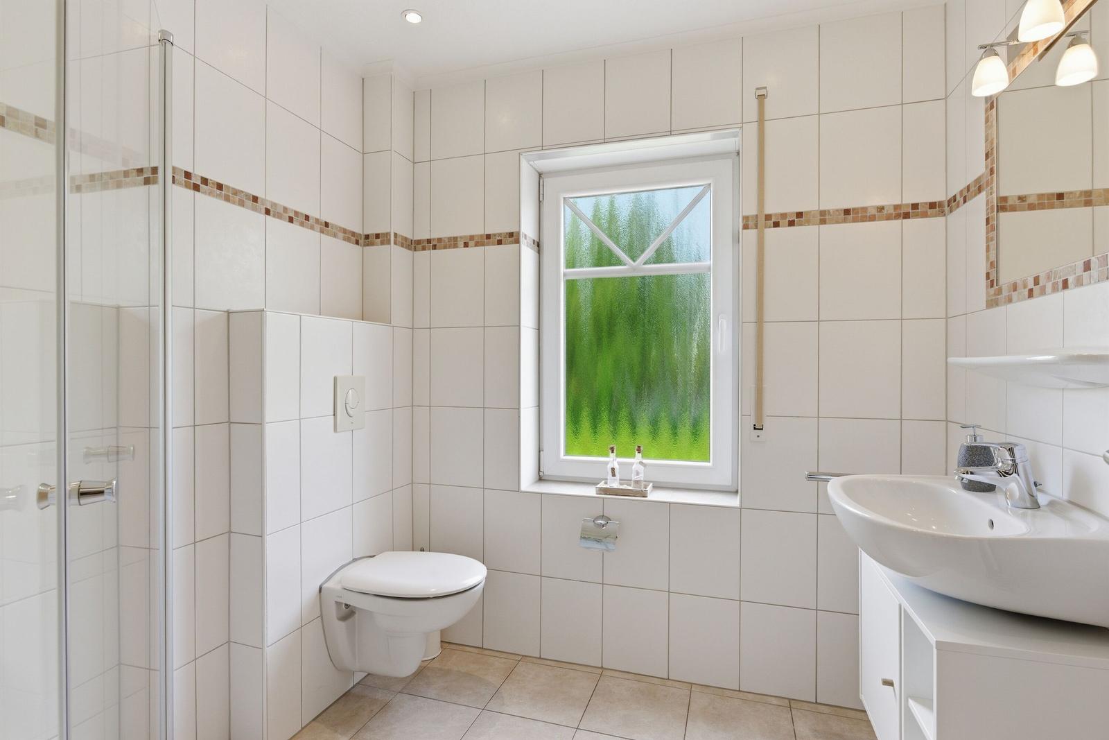 Badezimmer mit Dusche, Toilette und Waschbecken. Fenster mit grünem Glas.
