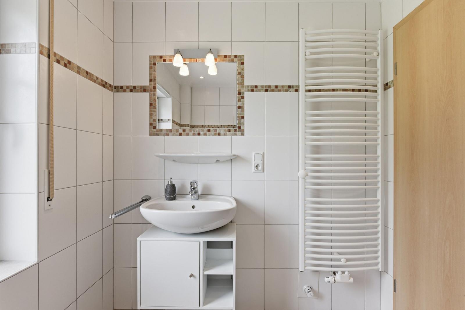 Badezimmer mit Waschbecken, Spiegel und Heizkörper an der Wand.