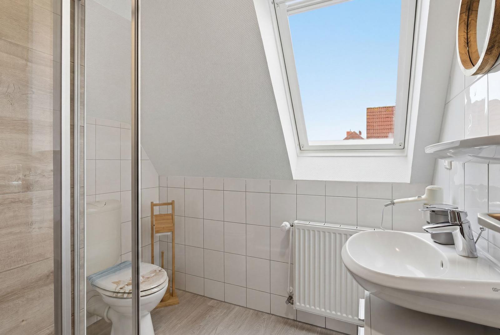 Badezimmer mit Dusche, Toilette und Waschbecken unter Dachfenster
