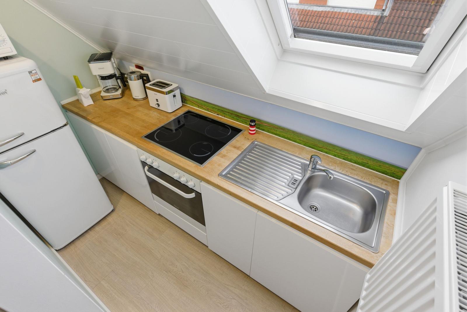 Küche mit Dunstabzug, Kühlschrank, Herd und Spüle unter Dachfenster.