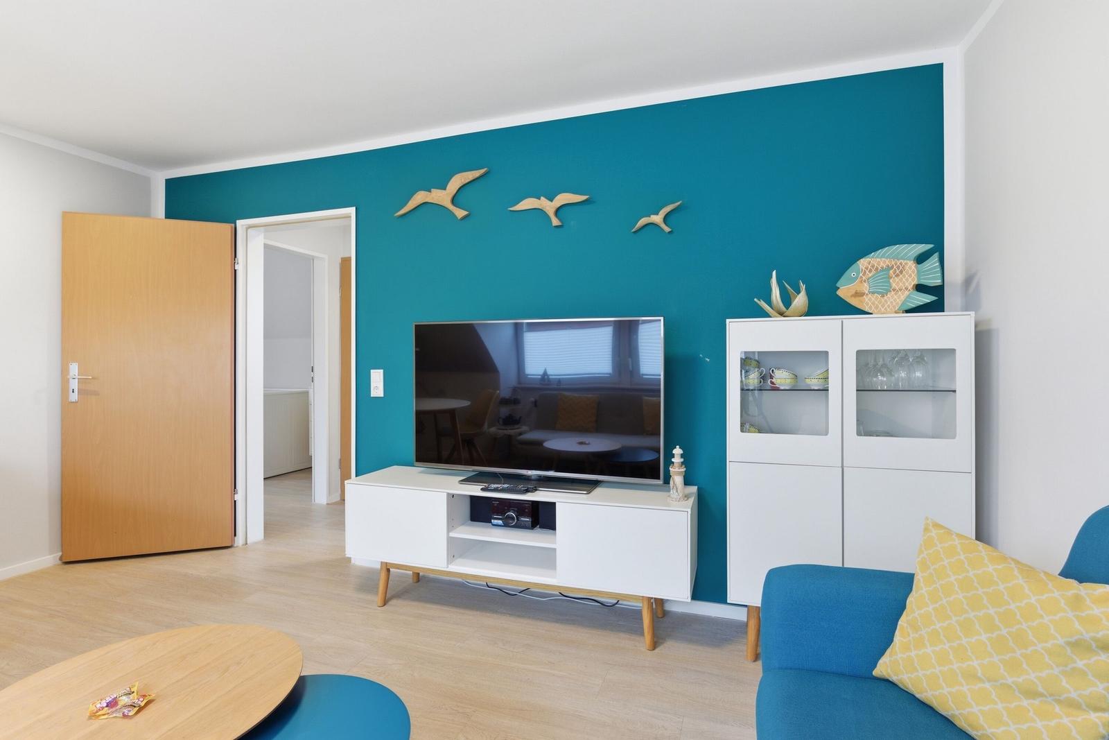 Wohnzimmer mit blauer Wand, Fernseher, Schrank und Sofa.