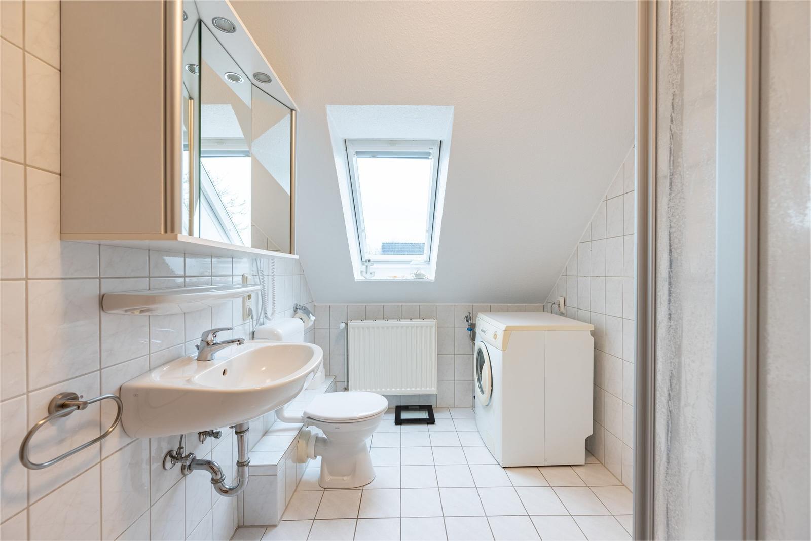 Badezimmer mit Waschmaschine, Toilette und Dachfenster.