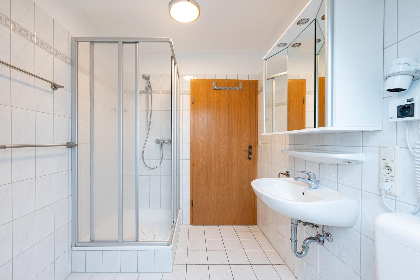 Badezimmer mit Dusche, Waschbecken und Spiegelschrank.